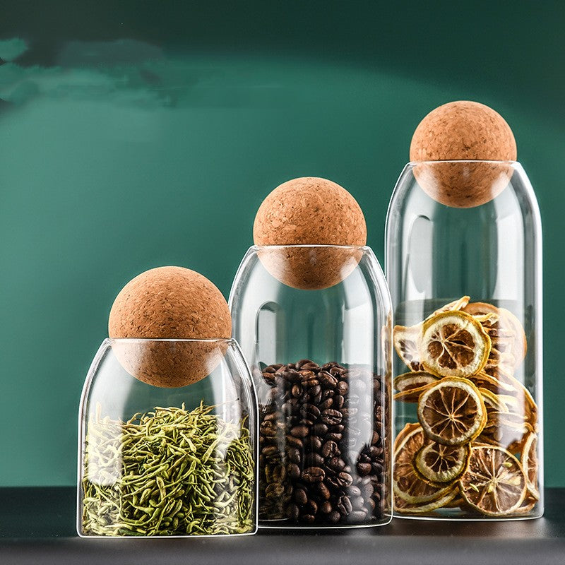 Three clear glass bottles with cork stoppers: dried herbs, coffee beans, and citrus slices