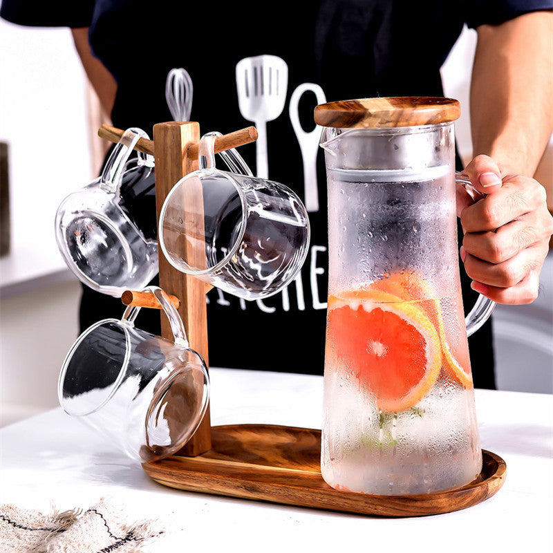 Glass cold water bottle with wood stand, metal lid, citrus slices and four glass cups
