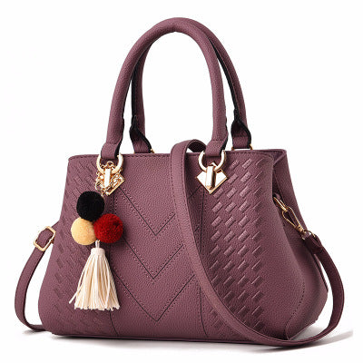 Purple quilt-textured handbag with top handles, crossbody strap, and pom tassel charm