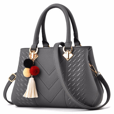Grey quilt-textured handbag with top handles, crossbody strap, and pom tassel charm