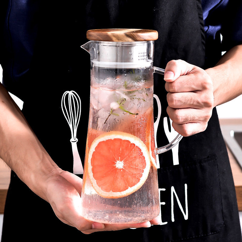 Glass cold water bottle on wood stand, metal lid, orange citrus slices in pitcher