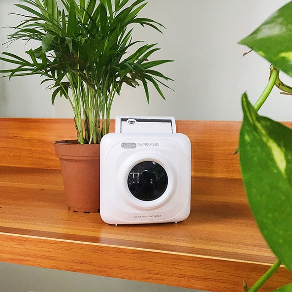 White mini mobile thermal photo printer on wooden table, front lens and slot