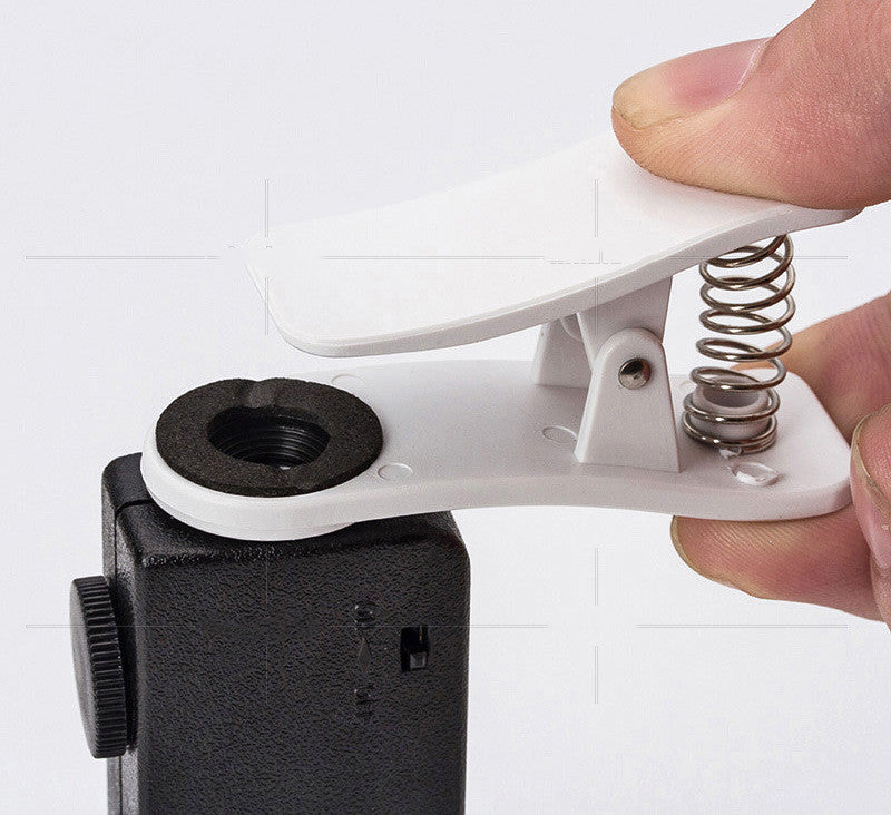 Hand holding white phone clip frame attached to black clip-on microscope