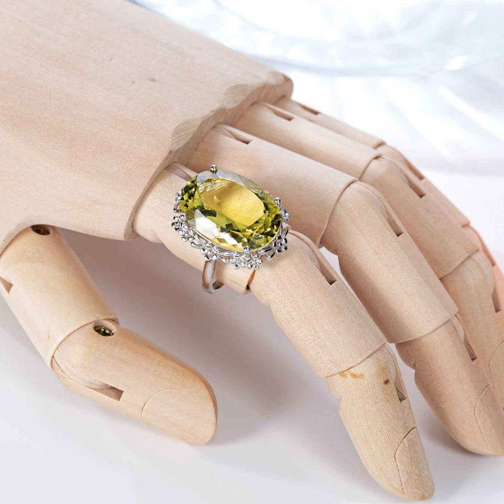 Yellow oval crystal ring on finger with silver side clusters and faceted center stone