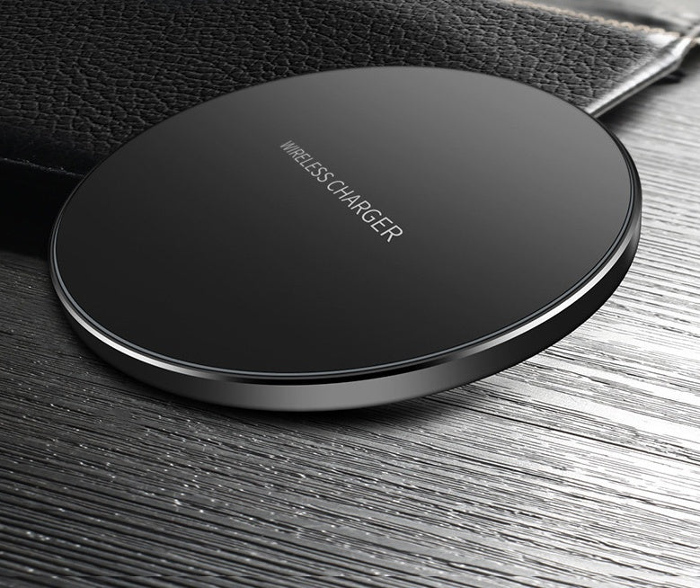 Black wireless charger pad on wood with faint printed text