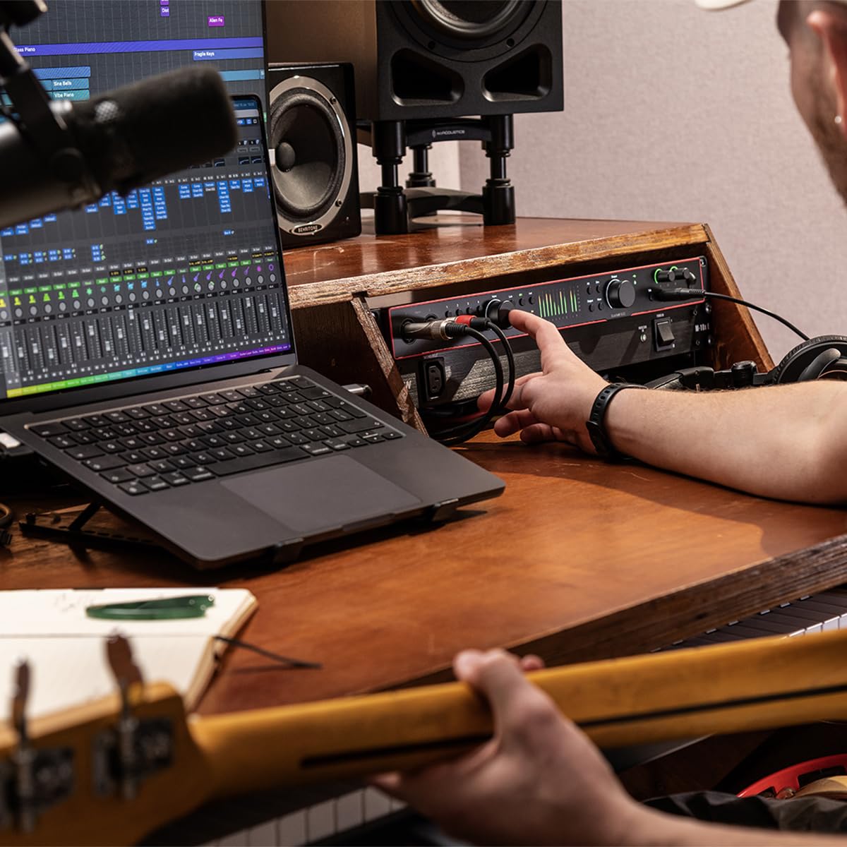 Focusrite Scarlett 18i16 USB audio interface on desk with hand reaching controls and connected cables