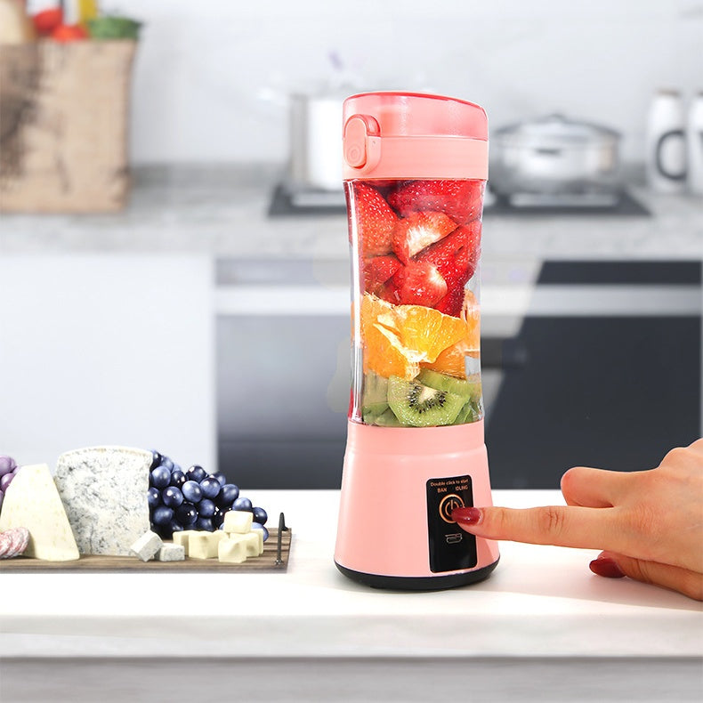 Pink portable electric fruit juicer with clear blending cup filled with fruit pieces