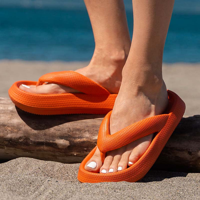 Orange thick-bottom flip flops on a sandy rock, wide thong straps