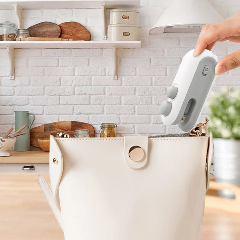 Handheld white vacuum heat sealer, gripped over storage bag in kitchen