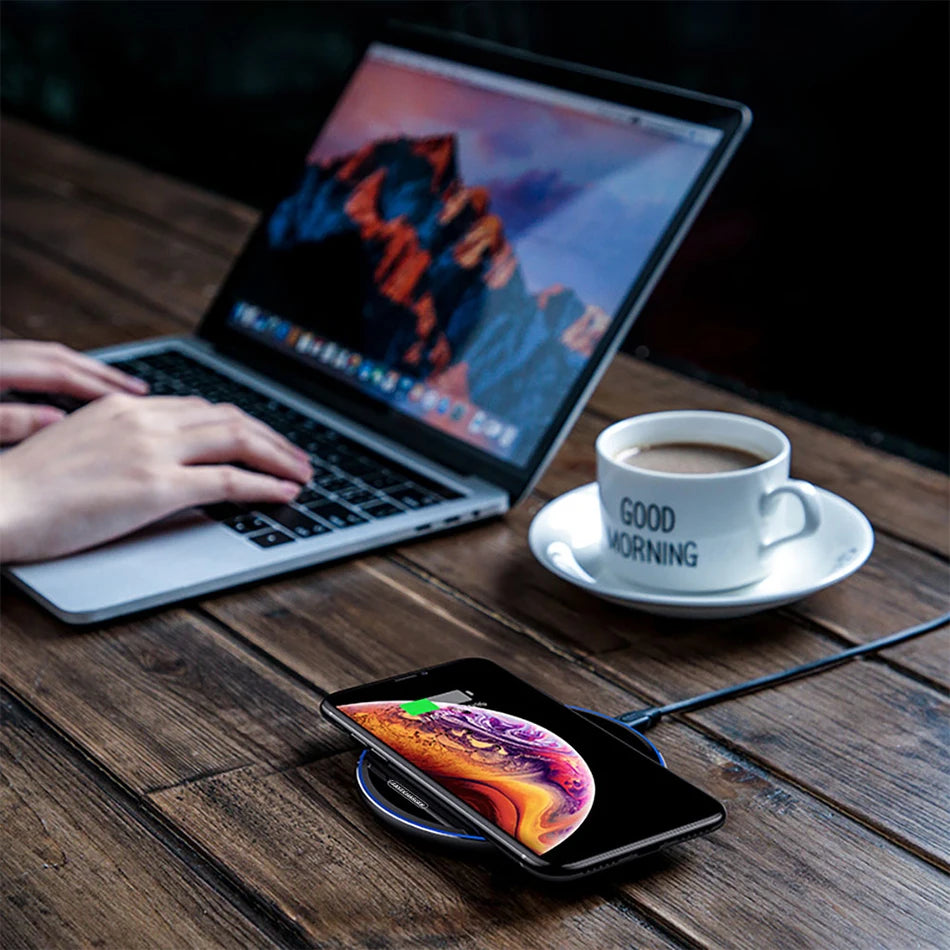 Black wireless charger pad on tabletop with phone resting on it