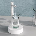 White electric water dispenser pouring water into clear glass cup, countertop base