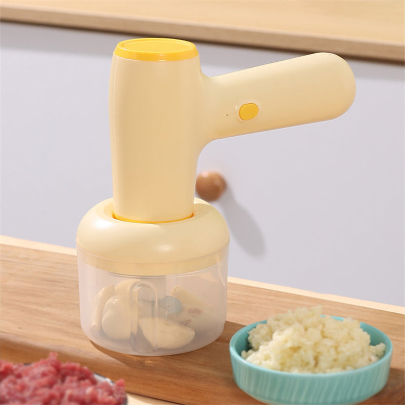 Beige electric chopper with clear cup and chopped garlic in blue bowl