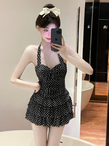 Black polka-dot one-piece swimsuit with bow halter neckline and flared skirt