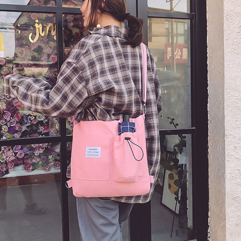 Pink canvas tote backpack with front pocket and drawstring, plaid patch detail