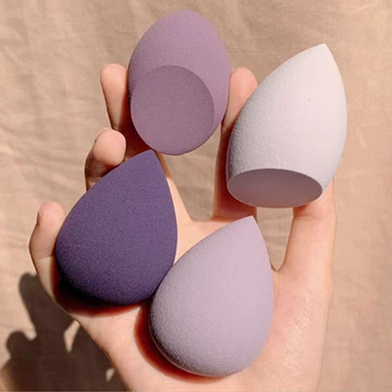 Teardrop makeup sponges in lavender, purple, and light gray, held in hand