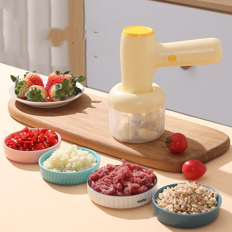 Beige electric chopper with clear cup and food bowls on wooden board